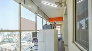 Un pasillo estrecho con amplios ventanales, un ventilador de techo y vistas de edificios al exterior.