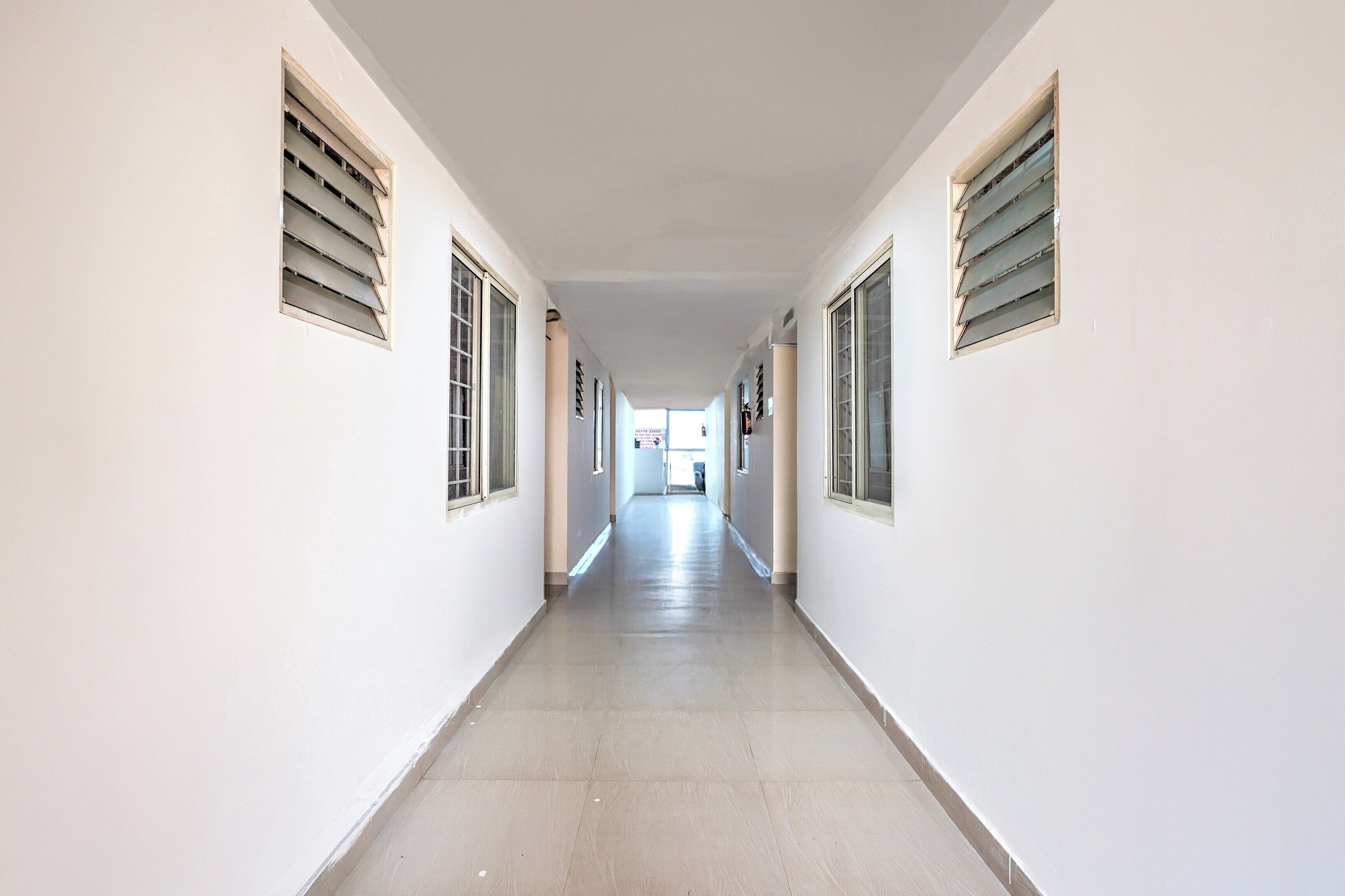 Um corredor comprido e estreito, com paredes brancas e chão de azulejos.