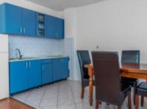 A kitchen with blue cabinets, a tiled backsplash, and a dining table with chairs. - Three Bedroom Apartment With Balcony and Sea View (Crikvenica)