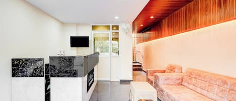 A modern interior with a reception desk, a flat-screen TV, a seating area with a sofa, and a staircase leading to an upper level.