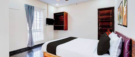 A hotel room with a bed, a ceiling fan, a TV, and artwork on the wall.