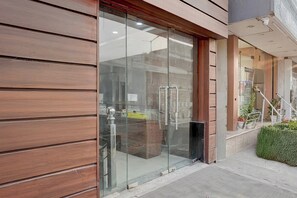 A modern building entrance with a glass door, wooden paneling, and a small step leading to a covered area with plants. - Collection O Haridwar Railway Station (Haridwar)