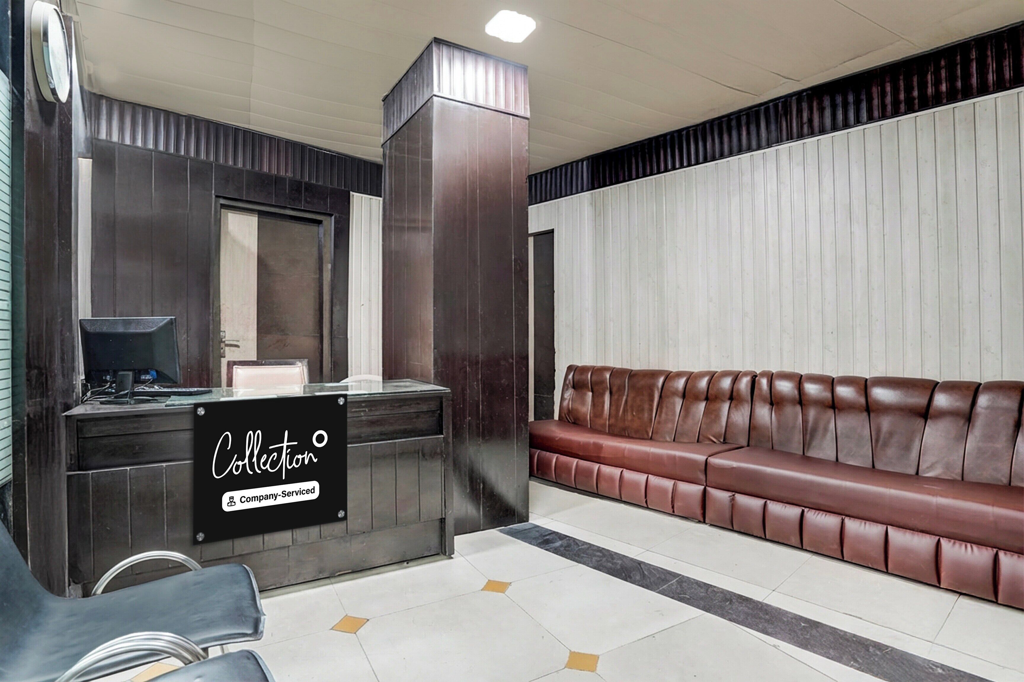 A reception area with a counter, a sign indicating company-serviced, a brown leather sofa, and a tiled floor.