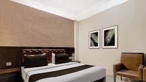 Ein modernes Schlafzimmer mit einem gesteppten Kopfteil, einem großen Bett mit schwarz-weißer Bettwäsche, einem braunen Ledersessel und zwei gerahmten Kunstwerken mit Blättern an der Wand.