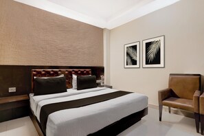 A modern bedroom with a tufted headboard, a large bed with black and white bedding, a brown leather armchair, and two framed leaf artworks on the wall. - Collection O Haridwar Railway Station (Haridwar)