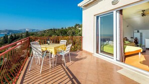 Ein Balkon mit Tisch und Stühlen, ein Bett mit grüner Bettdecke und Blick auf die Landschaft.
