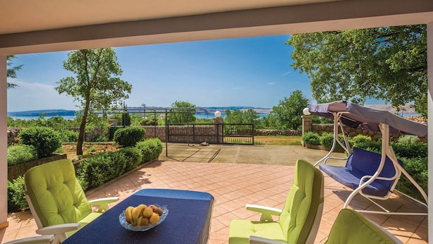 Um pátio externo com uma mesa posta para refeições, cadeiras e vista para o mar.