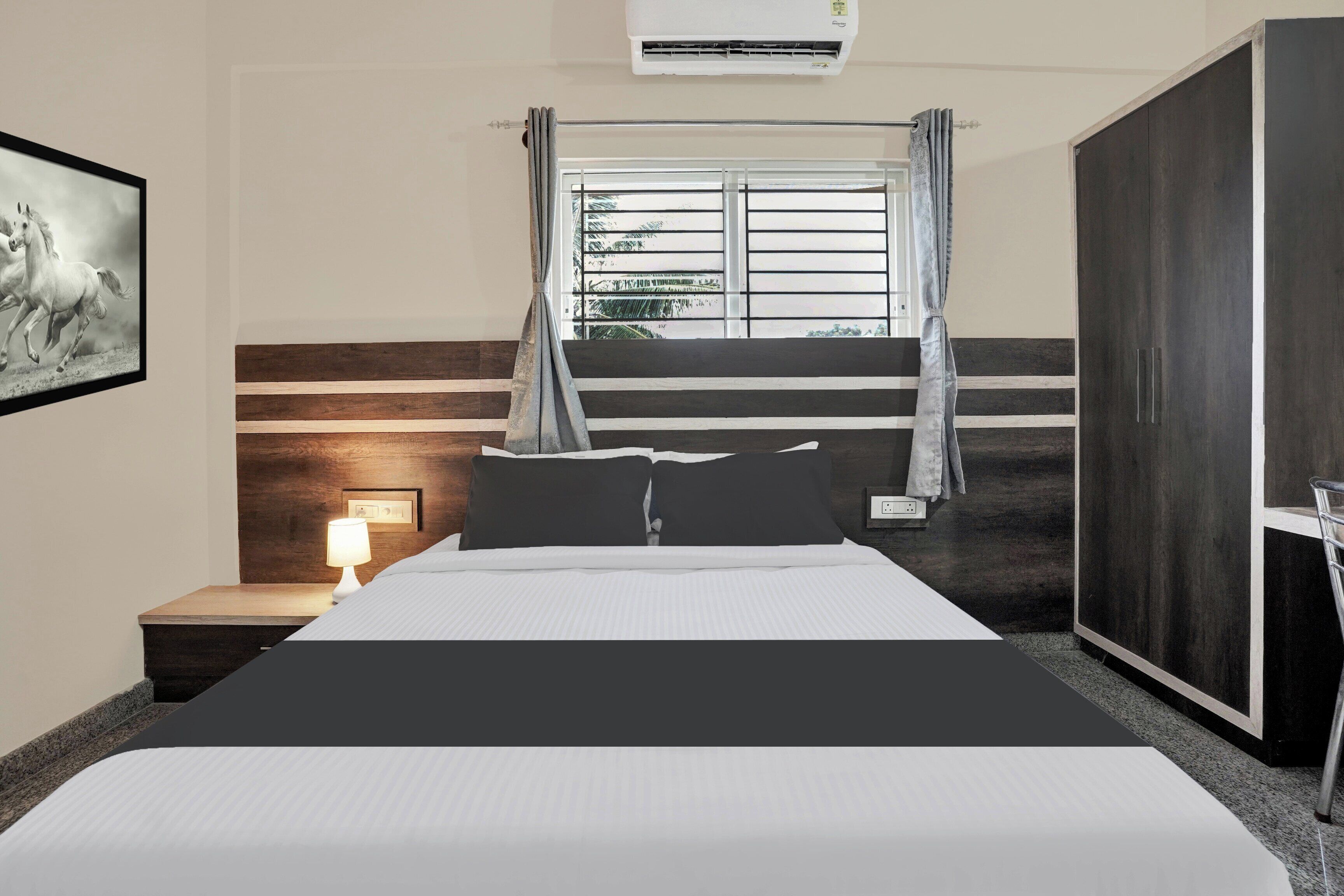 Habitación de hotel con cama, lámpara de noche, ventana con cortinas y equipo de aire acondicionado.