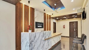 A hotel reception area with a marble reception desk, wooden paneling, a ceiling fan, and a fire extinguisher. - Collection O K R Puram (Bangalore)
