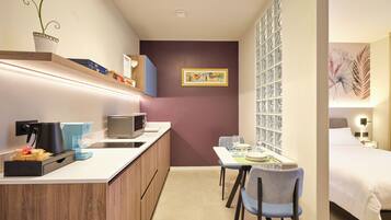 A compact hotel room with a kitchenette, a dining area, and a bed.