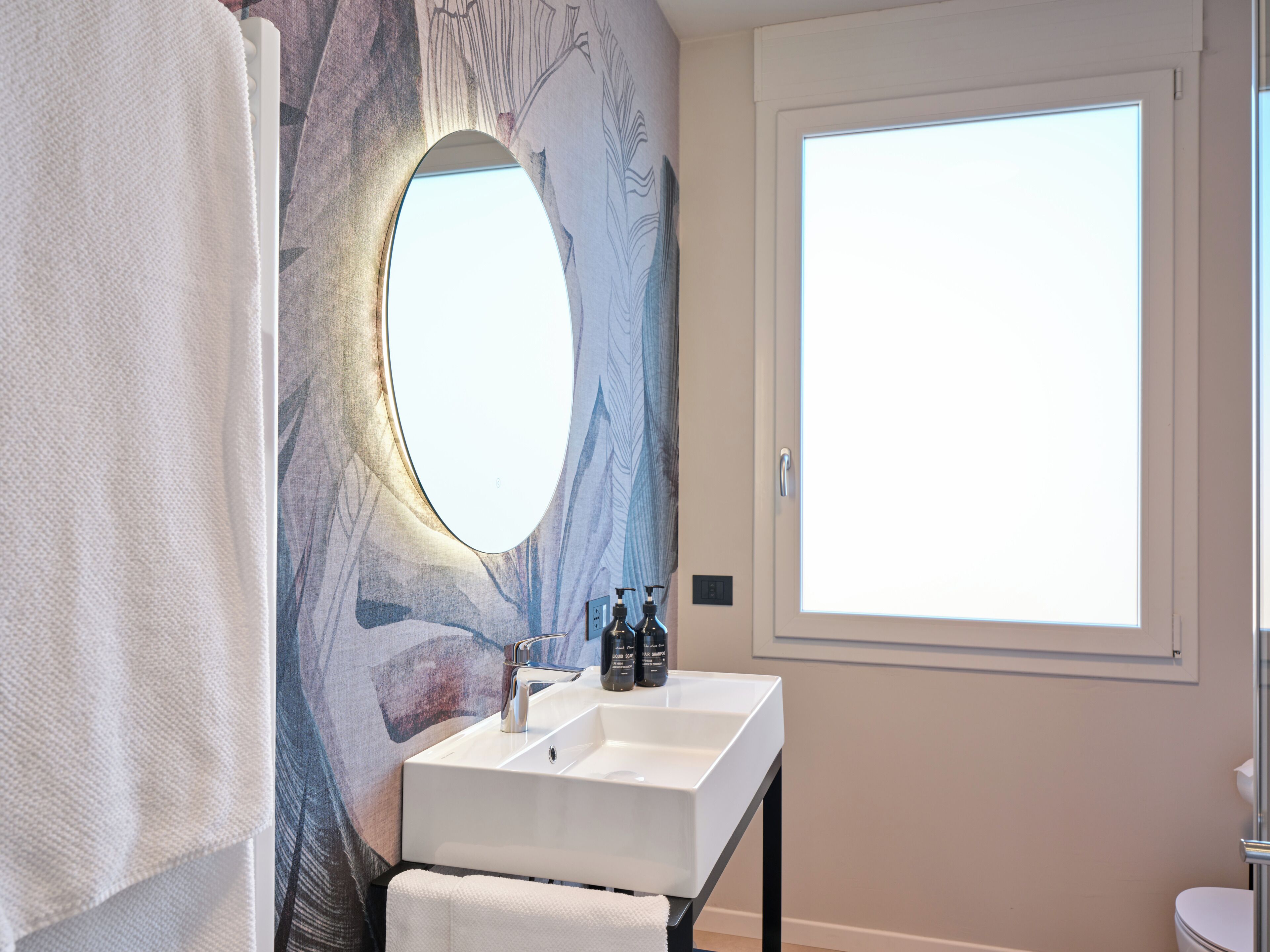 A bathroom with a white sink, a mirror, and a window.