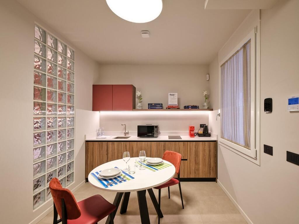 A compact kitchen with a dining area, featuring a round table, chairs, a microwave, and a small cabinet.