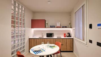 A compact kitchen with a dining area, featuring a round table, chairs, a microwave, and a small cabinet.
