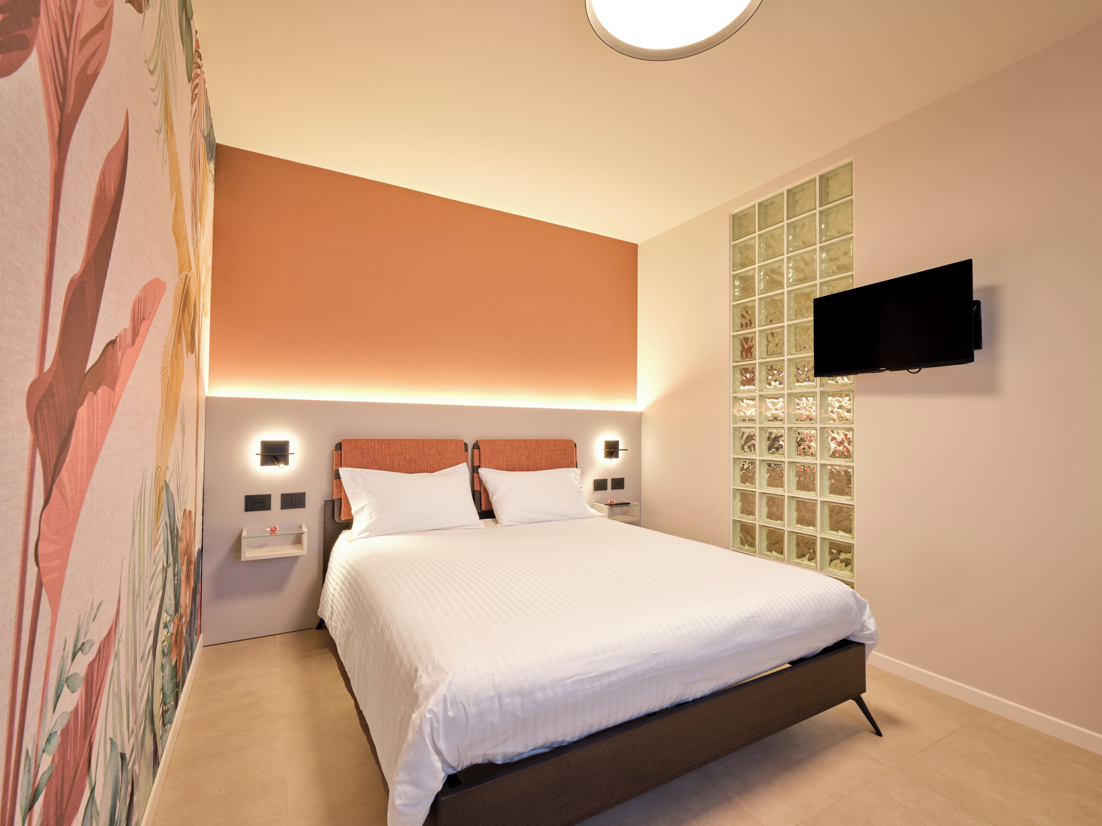 A modern hotel room with a bed, wall-mounted TV, and a decorative wall panel.