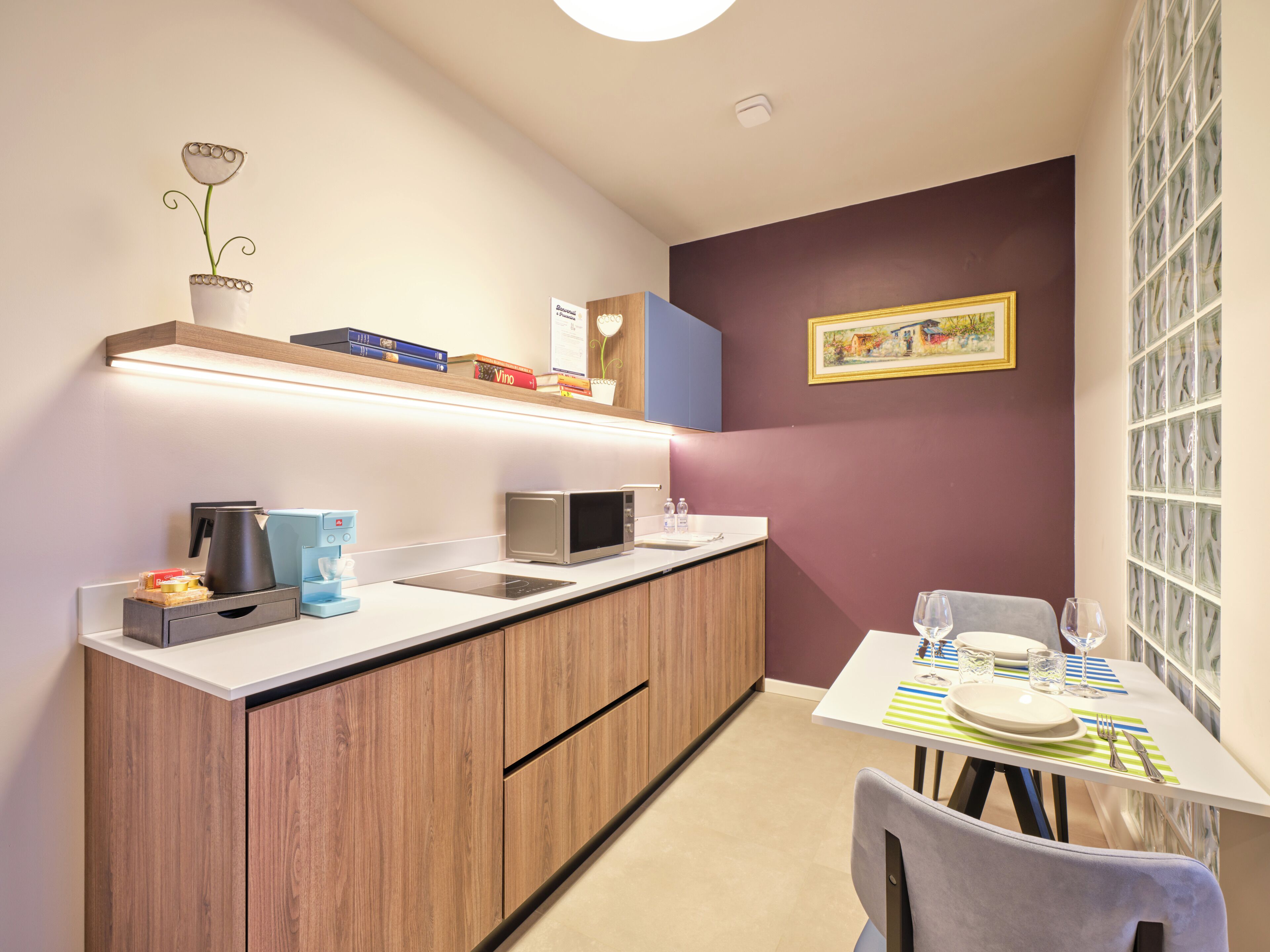 A compact kitchenette with a microwave, coffee maker, and a small shelf with books.