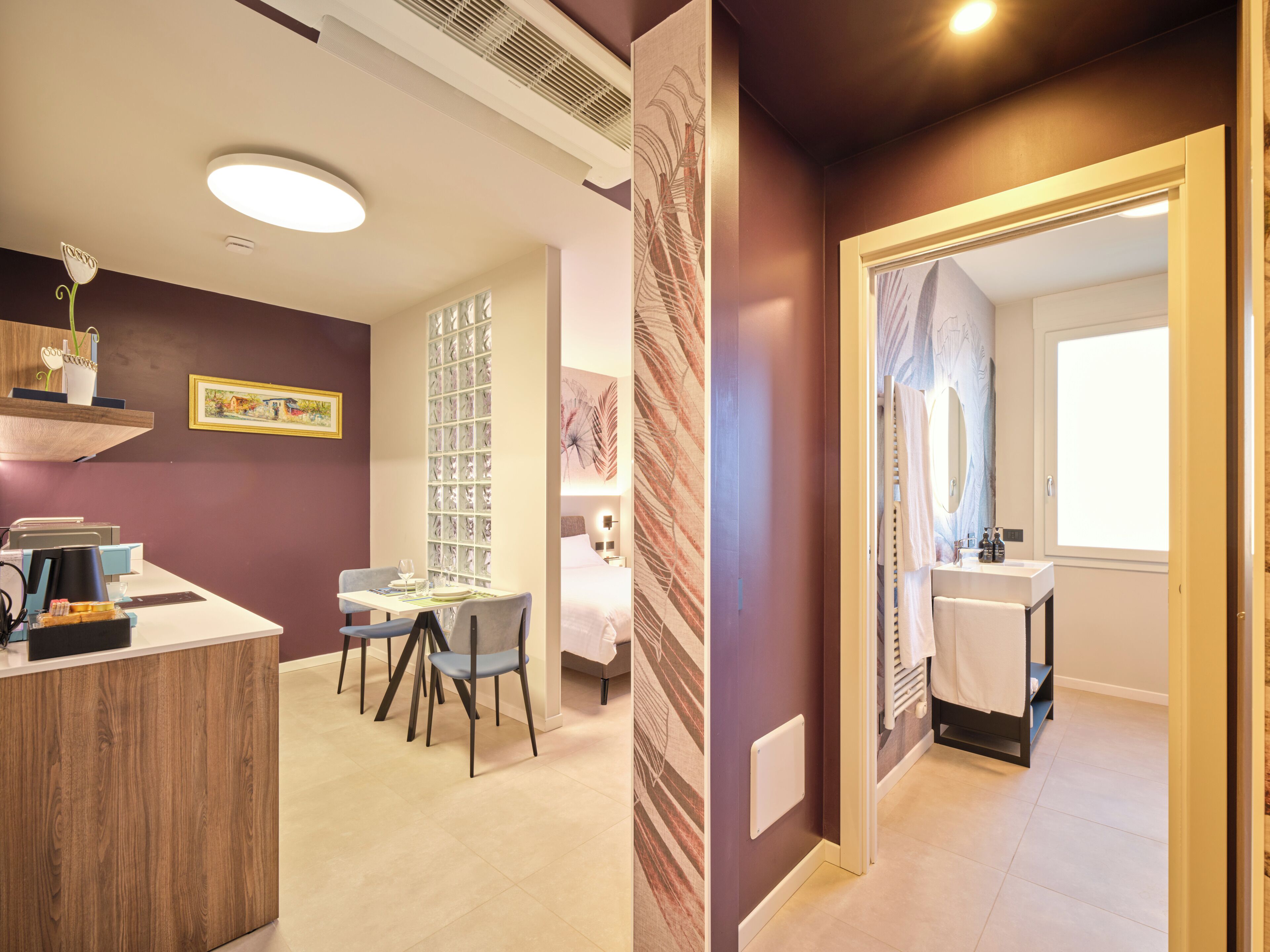 Quarto de hotel com área de refeições, banheiro com uma janela ampla e uma recepção.