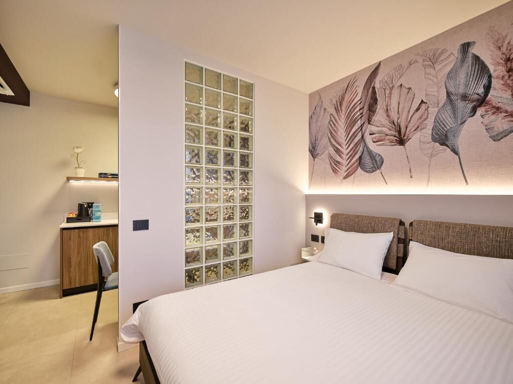 A hotel room with a large bed, a desk with a chair, a wall-mounted light, and a decorative panel with a floral pattern.