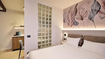 A hotel room with a large bed, a desk with a chair, a wall-mounted light, and a decorative panel with a floral pattern.
