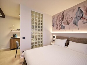 A hotel room with a large bed, a desk with a chair, a wall-mounted light, and a decorative panel with a floral pattern.