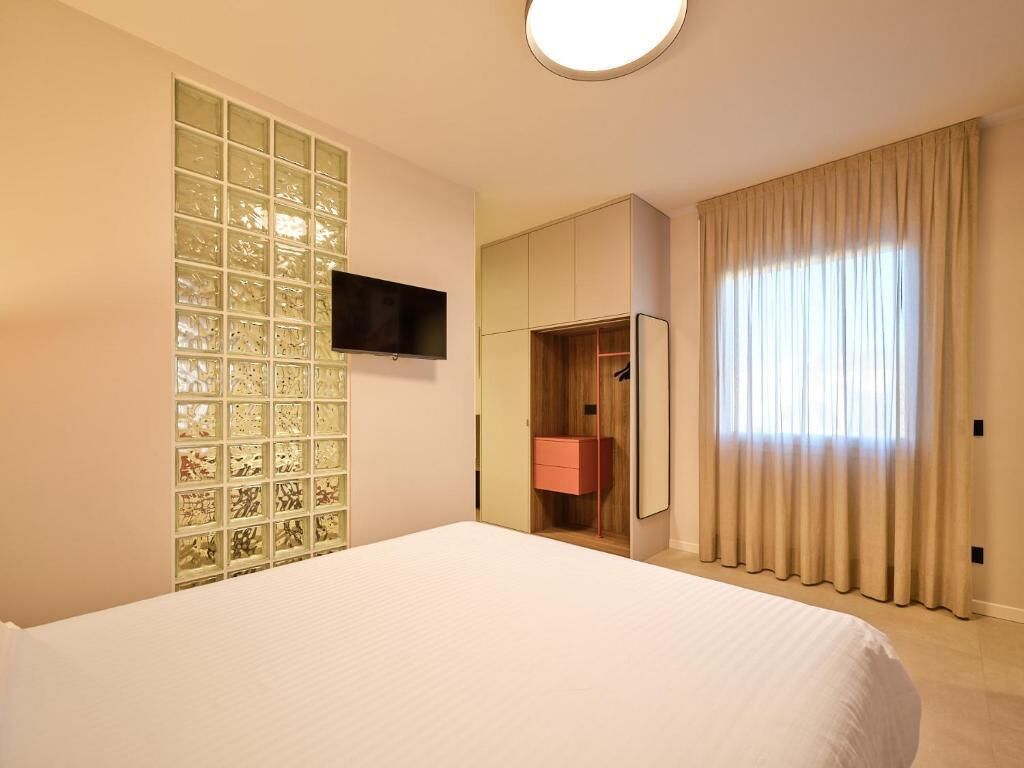 A hotel room with a large bed, a television mounted on the wall, a wardrobe, and a window with curtains.