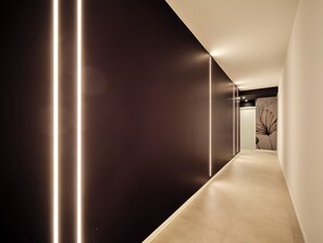 A modern hallway with a dark wall, a light floor, and a wall-mounted light fixture.