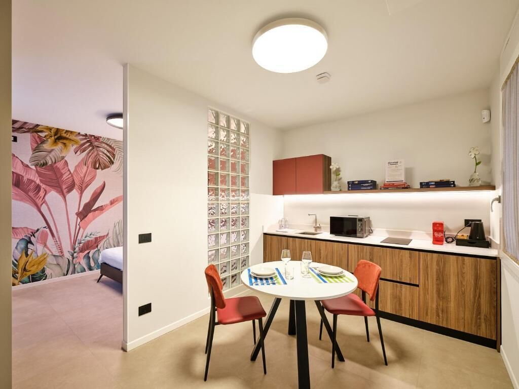 A modern kitchen with a dining area, featuring a round table with chairs, a microwave, and a coffee machine.