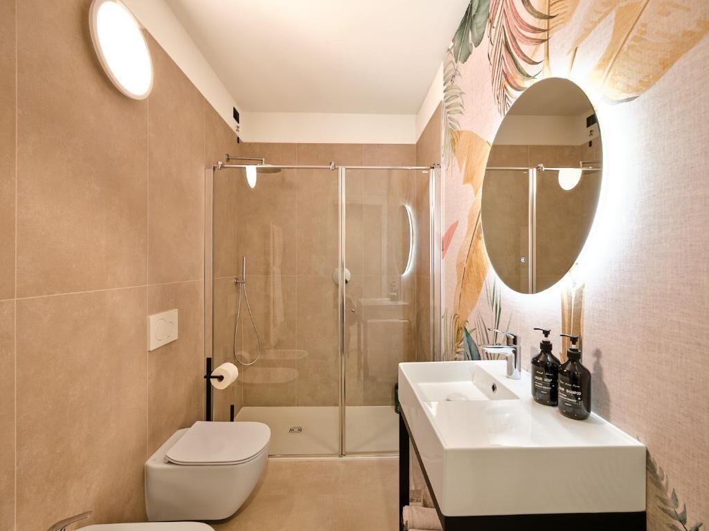 Ein modernes Badezimmer mit einer einteiligen Duschkabine, einer Toilette und einem Waschtisch mit Spiegel und zwei Shampoo-Flaschen.
