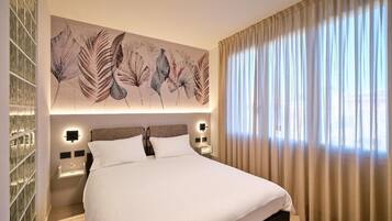 A hotel room with a large bed, a wall-mounted artwork, a nightstand, and a window with curtains.