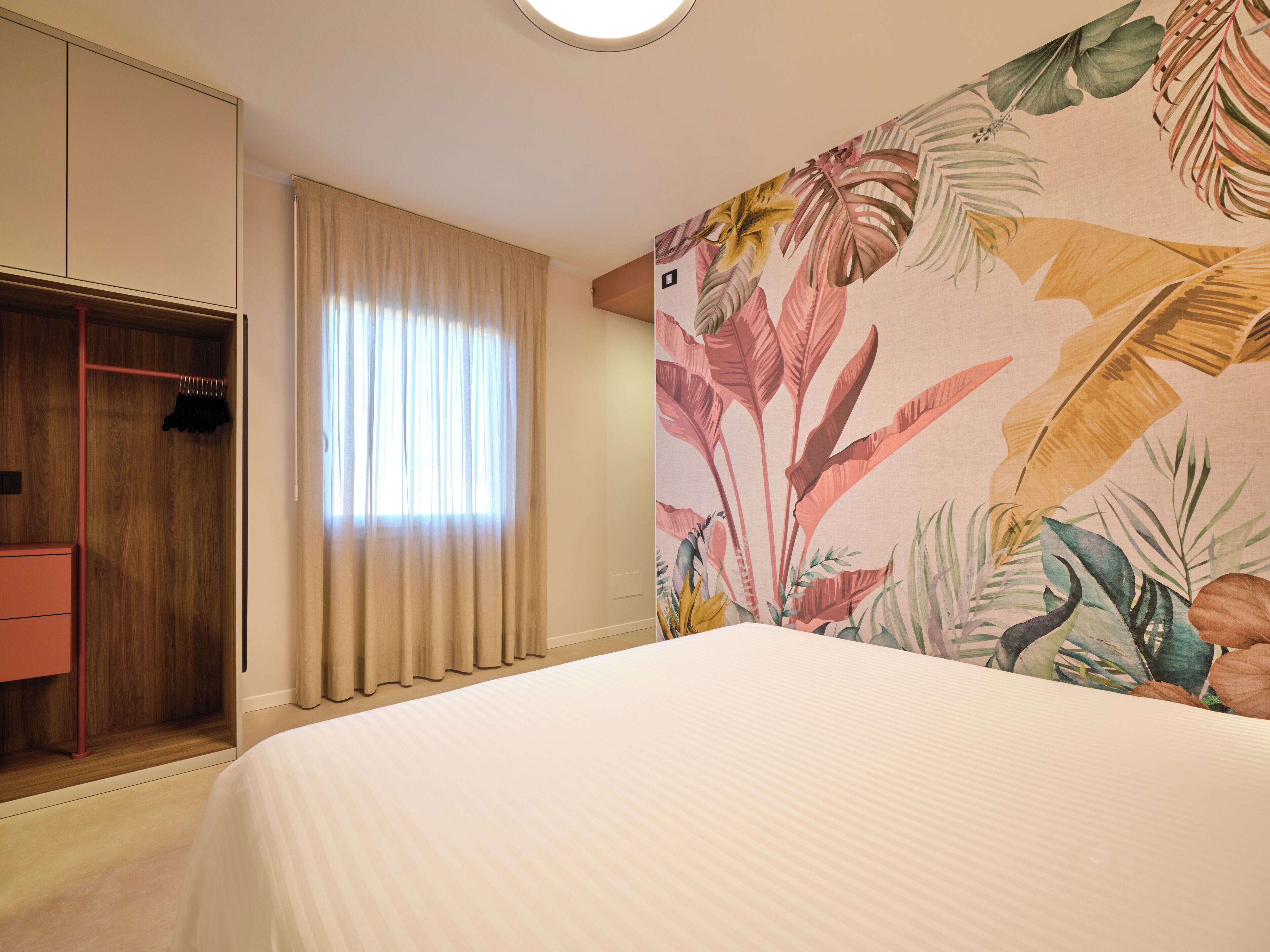 Una habitació d'hotel amb un llit, un armari i una finestra amb cortines.