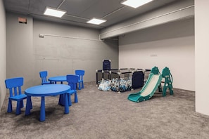 Ein Kinderspielbereich mit blauen Stühlen und Tischen, einer Rutsche und einem Ballbecken.