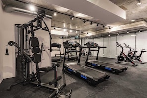 Ein Fitnessraum mit Laufbändern, einer Hantelbank und einem Kabelzuggerät.