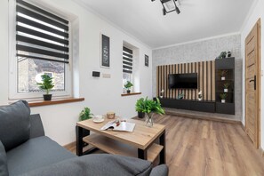 Een moderne woonkamer met een bank, een salontafel en een televisie bevestigd aan een houten wandpaneel.