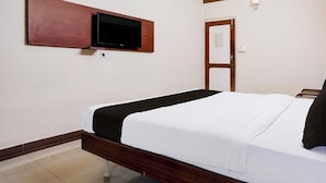 A hotel room with a bed, a flat-screen TV mounted on the wall, a wooden headboard, and a mirror.