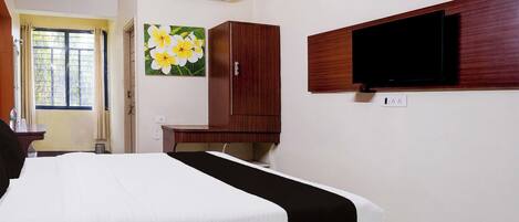 A hotel room with a bed, a television mounted on the wall, a wooden wardrobe, and an air conditioning unit.