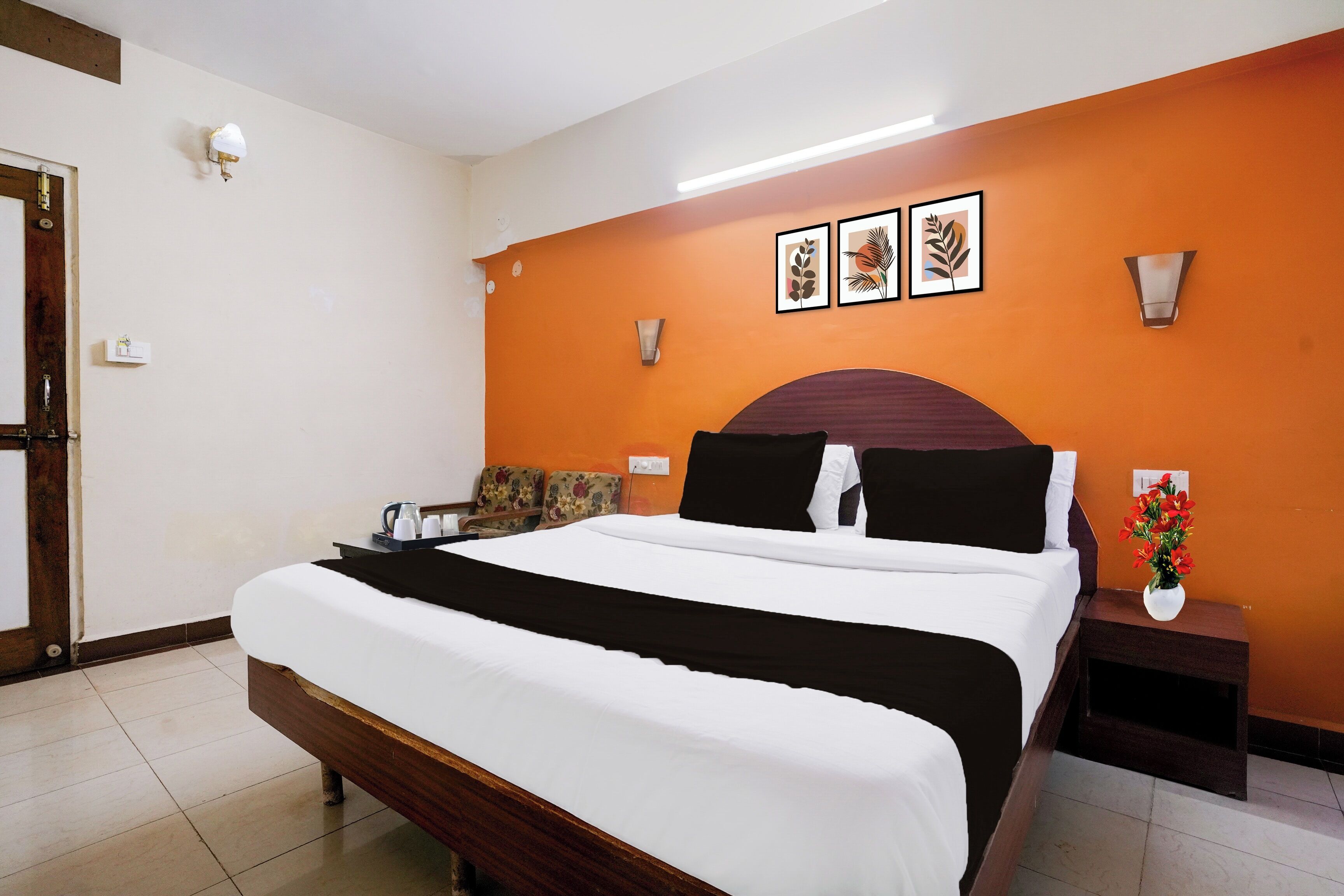A hotel room with a bed, a nightstand, a vase with flowers, and wall art.