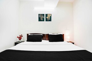 Habitación de hotel con una cama, dos mesitas de noche, una lámpara y dos obras de arte en la pared.