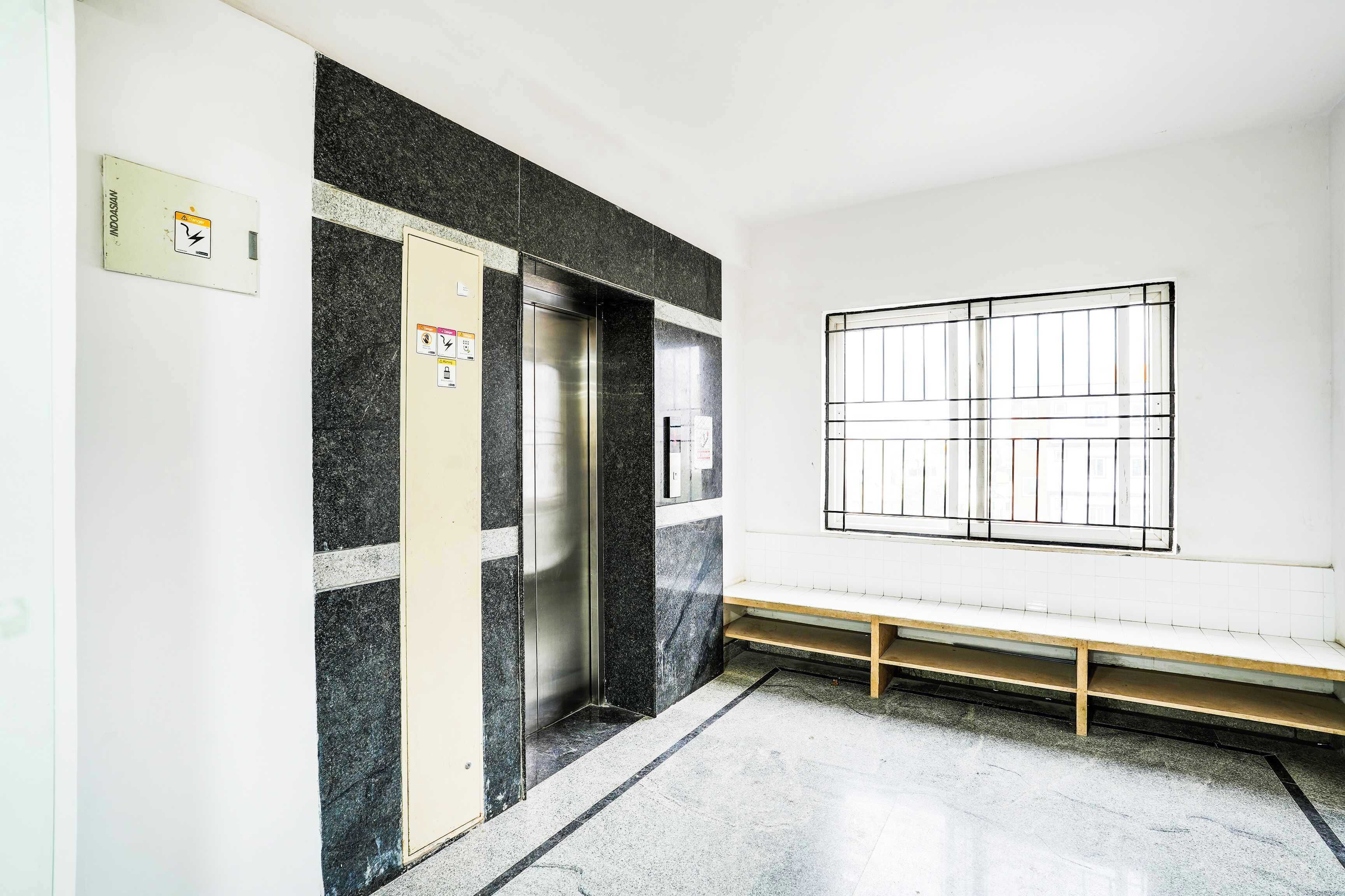 An elevator with a control panel, a bench, and a window with bars.