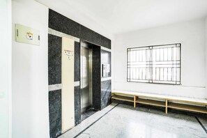 An elevator with a control panel, a bench, and a window with bars. - Collection O Peenya 2nd stage (Bengaluru)