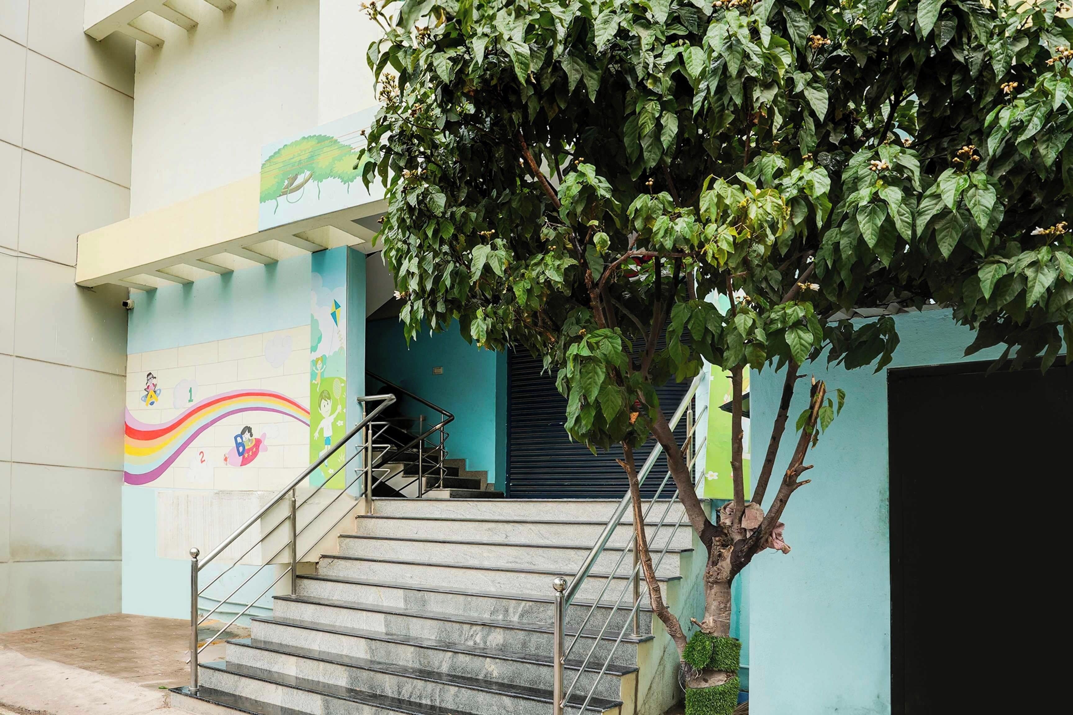 Un escalier menant à l’étage supérieur, avec une fresque murale, un arbre et une porte fermée.