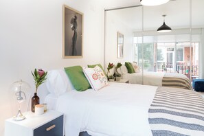 A modern bedroom with a large bed, bedside tables, a mirror, and a view of the outdoors. - Bright Homely 2BR in St Kilda East w Parking (Saint Kilda East)