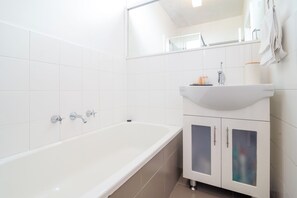 Un bany modern amb una banyera blanca, un lavabo amb un mirall a dalt i un moble amb portes.