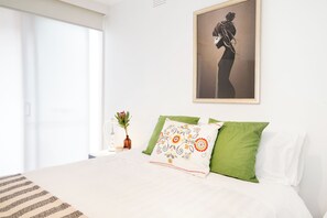 A bedroom with a bed, pillows, a vase with a flower, and a framed picture on the wall. - Bright Homely 2BR in St Kilda East w Parking (Saint Kilda East)