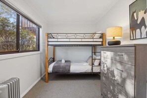 Una cama litera con cabecera, una lámpara de noche y un aparador con cajones.