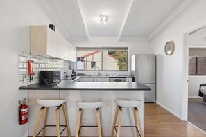 Eine moderne Küche mit einer zentralen Kochinsel, Barhocker, einem Feuerlöscher und einem Fenster mit Ausblick.