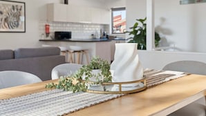 Eine moderne Küche mit weißen Schränken, ein Essbereich mit Holztisch und ein graues Sofa.