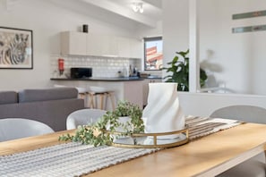 Eine moderne Küche mit weißen Schränken, ein Essbereich mit Holztisch und ein graues Sofa.