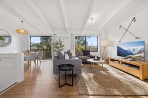 Ein modernes Wohnzimmer mit Sofa, Couchtisch, Fernseher und einem Essbereich mit Stühlen.