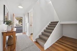 Un interior moderno con una escalera, suelo de madera y una pequeña mesa con una planta.
