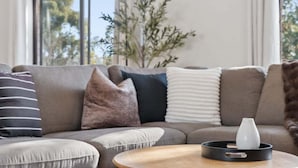 Ein modernes Wohnzimmer mit einem grauen Sofa, mehreren Kissen, einem runden Holztisch und einer Vase auf einem Tablett.