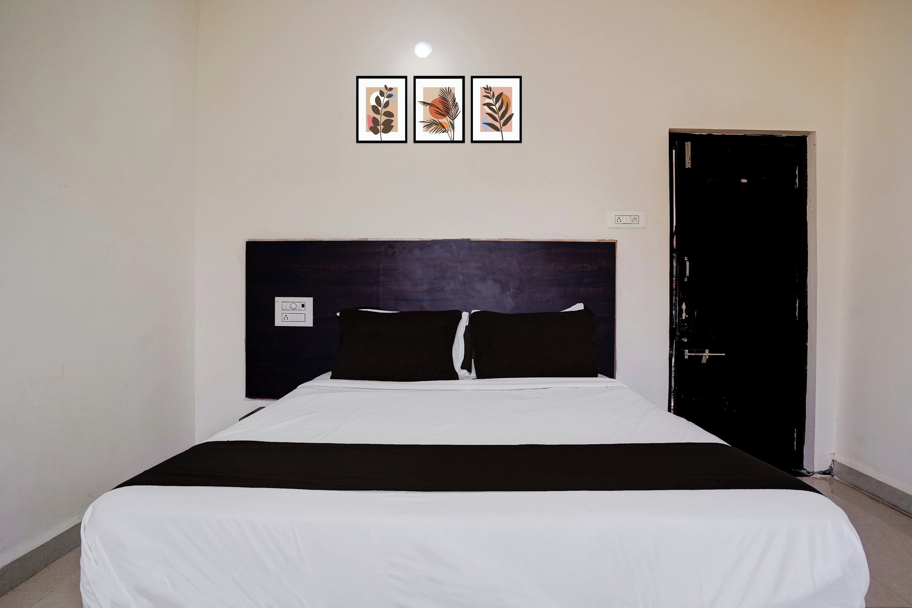 A standard hotel room with a bed, a black door, and three framed pictures on the wall.